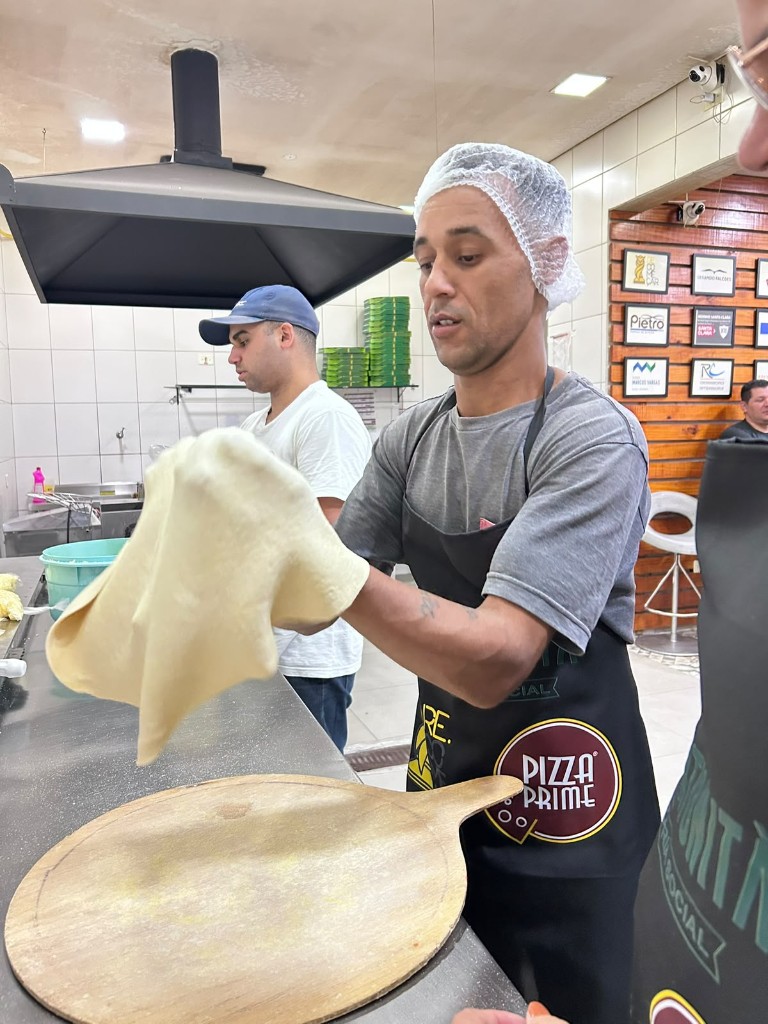 Aluno abre a massa de pizza sobre a pá de madeira na aula prática