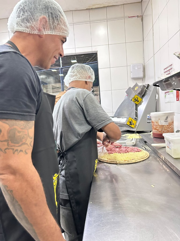 Alunos montam uma pizza com queijo e recheio na bancada da cozinha