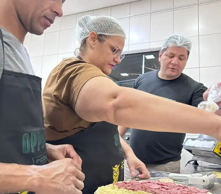 Equipe da Escola da Pizza coloca coberturas juntos sobre a massa