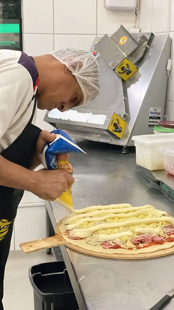 Pizzaiolo da Escola da Pizza aplica recheio cremoso sobre a pizza na cozinha