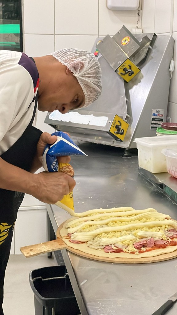 Pizzaiolo da Escola da Pizza aplica recheio cremoso sobre a pizza na cozinha