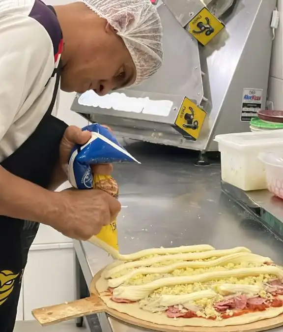 Pizzaiolo aplica recheio cremoso sobre a pizza na cozinha da Opportunità